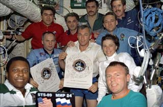 The STS-89 and Mir-24 crews pose with two versions of the flight roster, and the commemorative plaque. 